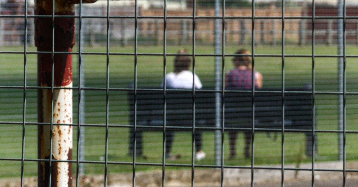 Two People discuss counselling outdoors in a therapeutic place, seen through a square mesh fence